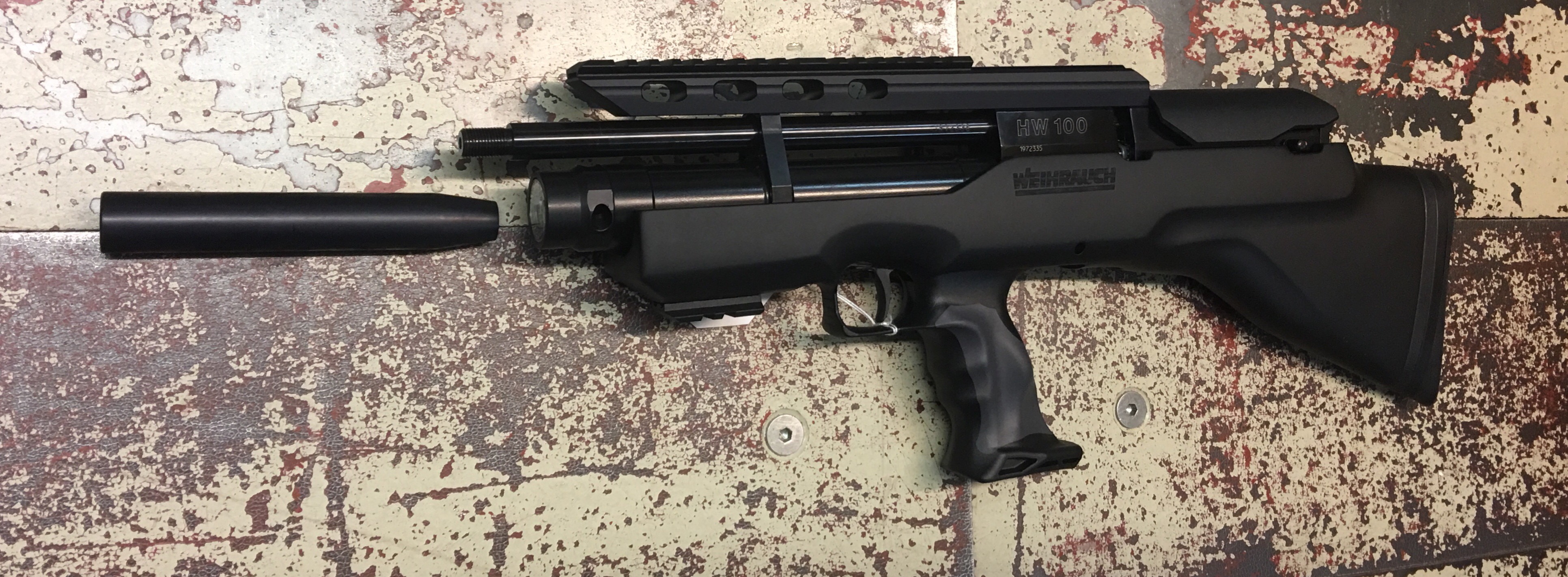 Hier ist das Luftgewehr Weihrauch HW 100 Bullpup-K, 31cm Lauf mit dem Laufgewinde gut zu sehen und daneben liegt ein Laufgewicht als mögliches Zubehör.
